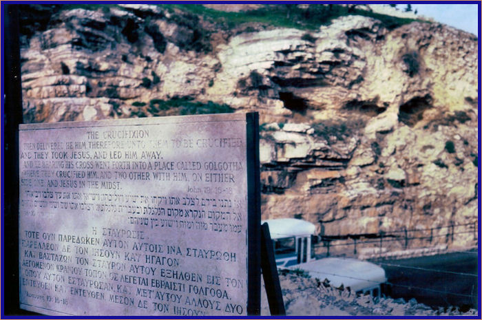 Sign written in English, Hebrew, and Greek quoting John 19:16-18 with Gordon's Golgotha in the background